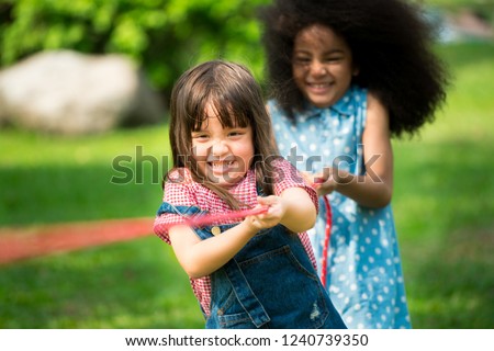 Happy children playing tug of war and having fun during summer camping in the park. Children recreation concept.