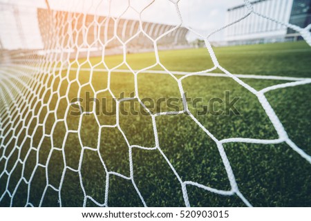 Soccer football net background over green grass and blurry stadium behind