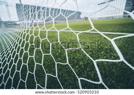 Soccer or Football Net Background, Viewed from Behind The Goal with Blurry Stadium and Soccer Field in the Background.