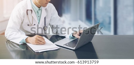 Male doctor working on desk with laptop computer and doctors paperwork on doctor desk. Medical, doctor concept by doctor on computer in doctors office with doctors stethoscope on doctors hospital.