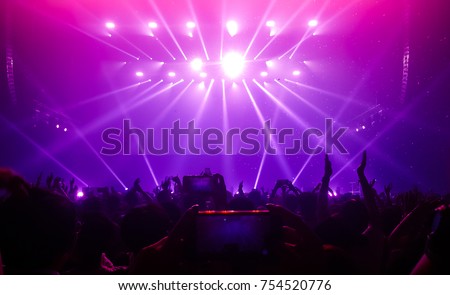 Happy people dance in nightclub party concert and listen to music from DJ on the stage in background. Cheerful crowd celebrate Christmas and New Year party 2018. Young people lifestyle and nightlife.