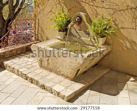 Fountain with lion head in sunny corner of French village square