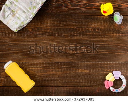 disposable diaper, teether, dummy, baby powder and rubber duckling on dark wooden background with copy-space. Flat lay