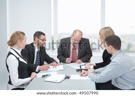 Group of businesspeople formed of men and women in an office at a table. Two of them sign a contracts.