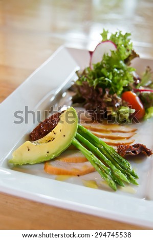 An appetizer with chicken slice and salad of avocado, asparagus, lettuce and baby plum tomato