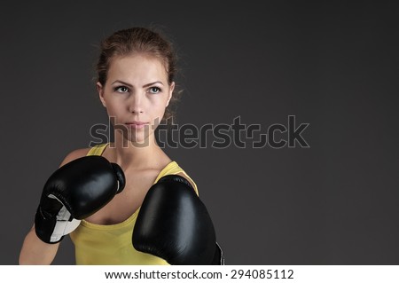 aggressive fight posing  beautiful young caucasian yellow top girl with black boxing gloves on dark gray background