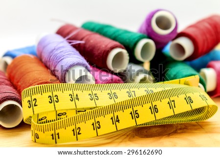 heap of sewing color bobbins threads and measure tape on wooden table with blur background