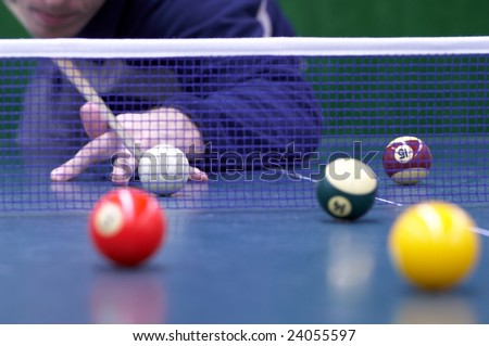 Player is preparing to make the hit overcoming the ping-pong net. the billiard with snooker balls is played on ping-pong table. Selective focus on white ball.
