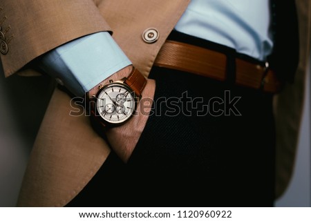 Closeup fashion image of luxury brown  watch on wrist of man.body detail of a business man.Man\'s hand in pants pocket closeup at white background.Man wearing beige jacket and white shirt.Not isolated