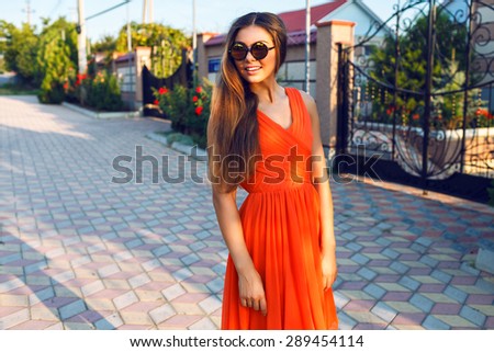Close up summer fashion Portrait of young pretty woman posing at countryside, wearing stylish bright orange dress and mirrored sunglasses, warm pastel colors.