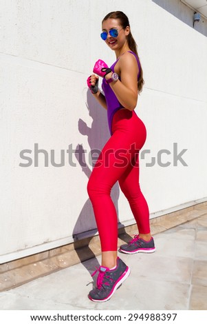 Strong sexy sportive woman with tan skin and long brunette hair wearing violet swimsuit and pink leggins,sport shoes,???? ?????? and blue glasses,doing outdoor boxing exercise at white background