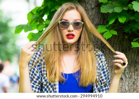Portrait of young teenage girl with long blondy hair. Attractive young woman in hipster outfit walking in a park on a sunny day. Taking rest on the summer lunch break. Young woman looking exciting.