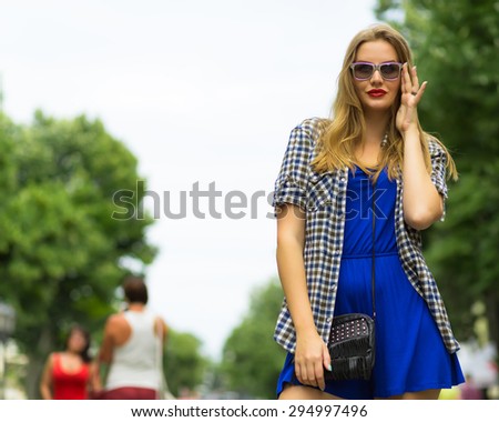 Portrait of young teenage girl with long blondy hair. Attractive young woman in hipster outfit walking in a street a sunny day. Sightseeing of a new city.  Wearing stylish blue suit, shirt and glasses