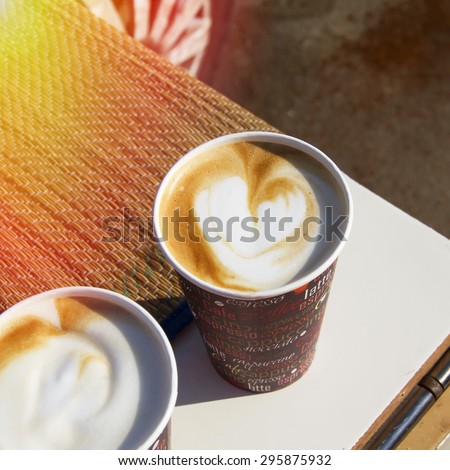 Morning cup of coffee with milk with heart shape made of foam. Outdoor coffee break in summer sunny day.