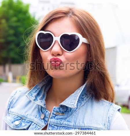 Young attractive fashionable surprised woman wearing glasses. Beautiful brunette woman with fresh make up and big lips, wearing stylish hipster summer outfit,street background. Sending kisses,get fun