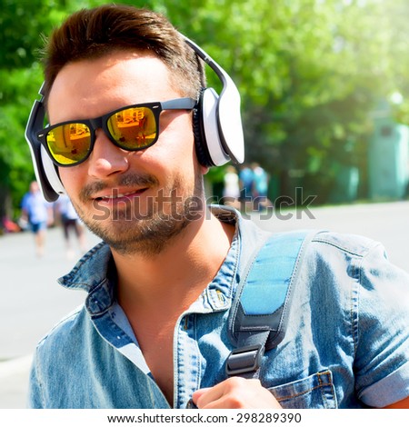 Summer close up fashion portrait of Handsome hipster modern man with wireless headphones traveling in Europe.  Portrait of a young handsome man with toupee and headphones in urban background.