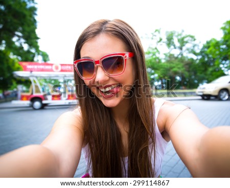 Close-up of trendy funny girl face in sunglasses making selfie photo pretty girl having fun showing tongue tourist takes travel selfie in Odessa.Outdoor portrait of pretty student girl taking selfie