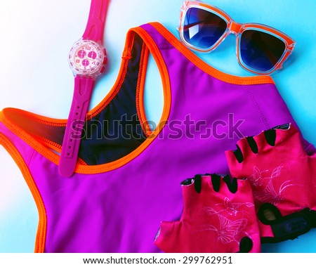 Sport clothes and all you need for training.Fitness accessories .Watch, sports bra top, sunglasses and sport gloves. Pink and orange sport wear on blue background. Top view.