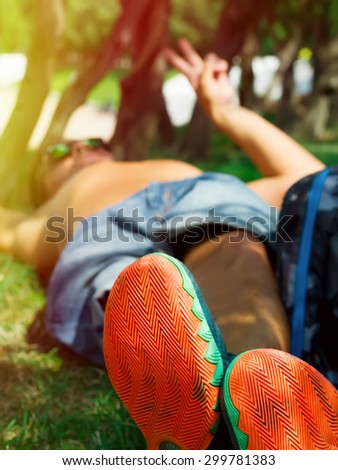Man relaxing in the grass.Focused on sport shoes.Man\'s feet relaxing on the grass. stylish young man sitting on grass.man taking a break and relax in a meadow in the wonderful warm light of sunset
