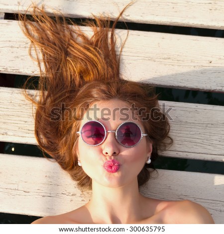 Close  up fashion portrait of teenage girl.Top view of a woman lying on her back, blowing a kiss.Indoor lifestyle or fashion portrait of stylish teenage model with curled red amazing hair,having fun.