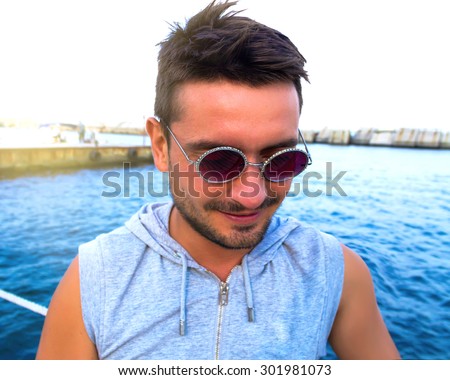 Portrait of a handsome male model posing at the seaside in funny sunglasses.young handsome man smiling in the beach.Hipster style guy.Stylish male haircut.Man enjoying beautiful view,relax near ocean.