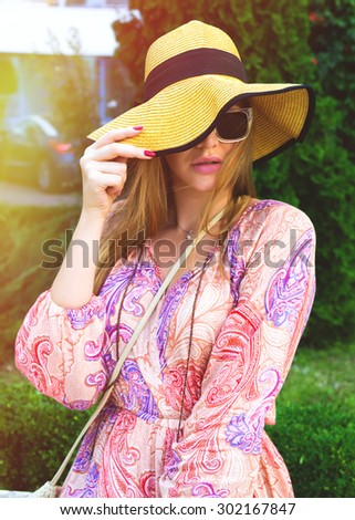 Young beautiful woman in floral fashion dress,big wide hat and sun glasses.Beautiful young fashion woman posing in park on sunny day.Vogue style. Romantic,elegance,confidence concept.Summer vacation
