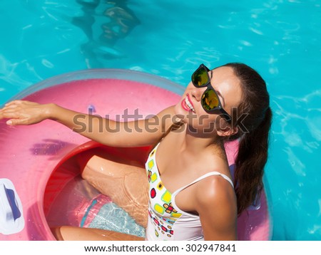 Beautiful sexy young woman with perfect slim figure with long dark hair and wet bathing suit fashion in stylish glasses from the sun is sunning by swimming pool swim, sunbathe have fun at pool party
