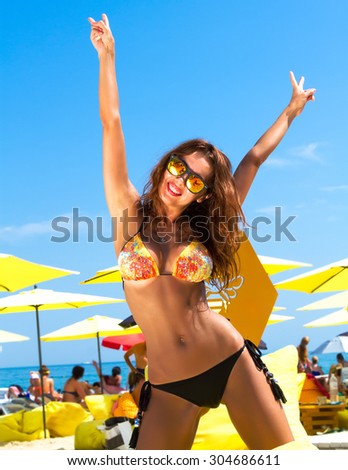 Summer fashion photo of beautiful tanned woman with brunette hair in sexy bikini relaxing at luxury beach resort on yellow beach chair. Summer close up of slim sexy woman going crazy on vacation.
