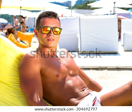 Portrait of a handsome young muscular man in white swimtrunks with luxury beach resort background