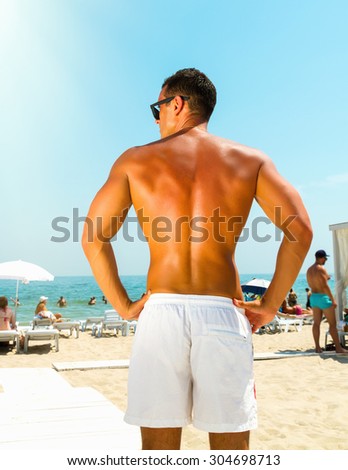 Young sexy man relaxing on the beach. Handsome muscular tanned young man on the beach view from the back