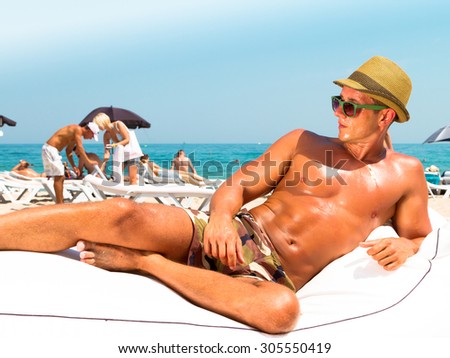 Portrait of a handsome young muscular man in military printed trousers and hipster retro straw hat in luxury beach resort,laying on beach chair ,relaxing getting fun and sunbath  on summer vacation