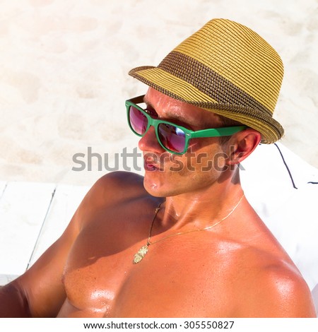 Sexy hot muscular Man on beach ,wearing hipster hat, sunglasses.Young male model enjoying summer travel holiday by the ocean on luxury beach resort