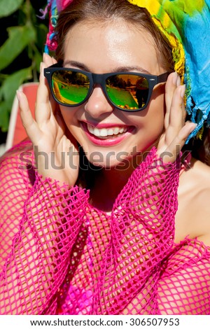 Outdoor close up fashion portrait of young sexy smiling woman with perfect bronze tanned skin with pink lips and white teeth in bright pink beach dress and mirrored glasses.Holiday party.Luxury