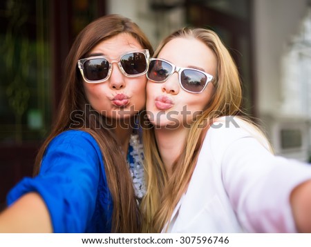 Close up lifestyle selfie portrait of two young positive woman having fun and making selfie, teenage hipster trendy clothes and sunglasses, long hairs,fresh make up. happy together. sisters, friends