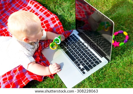 Cute baby boy playing with laptop and toys outdoors on green grass.Wondered baby looks at notebook screen.little boy playing outdoors with a laptop.baby boys face getting into on a laptop computer