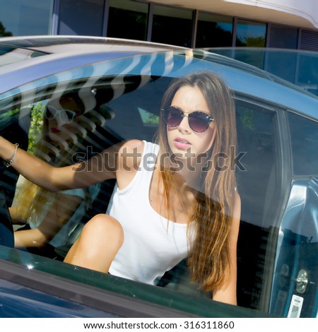 Young woman sitting in car.Portrait of Young teenage brunette student girl sitting driver seat in luxury blue sport car.Slim cute brunette woman inside black leather chair auto open door and going out