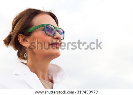 Fashion autumn close up portrait of Happy mature woman looking in to the sky,isolated on white.Looking forward,side view. Brunette woman wearing white jacket and green sunglasses,tanned,fresh make up