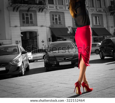Woman wearing red elegant skirt  and red high heel shoes in old town.Young beautiful business sexy woman walking,urban background.Back view of a fashion shopper woman legs. Black and white concept.