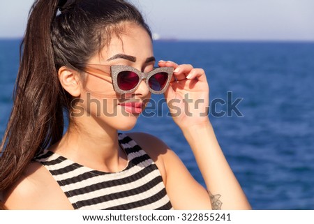 Summer fashion close up portrait of young woman looking to the ocean,enjoy her freedom and fresh air,wearing striped dress and vintage sunglasses at sea background.Beautiful girl  at summer beach.