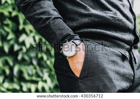 closeup fashion image of luxury watch on wrist of man.body detail of a business man.Man\'s hand in a grey shirt with cufflinks in a pants pocket closeup. Tonal correction