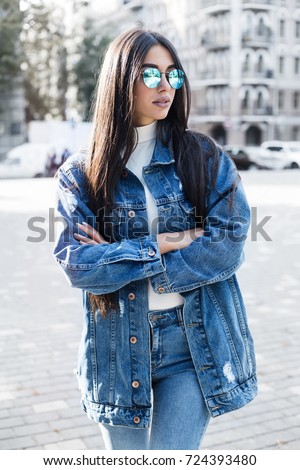 Hipster girl wearing blank gray t-shirt, jeans and backpack posing against rough street wall, minimalist urban clothing style.Stylish happy young woman wearing boyfriend jeans and long jeans coat