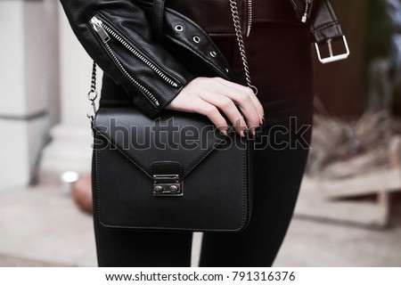 detail of a fashionable woman wearing short leather jacket,black purse,watches,black jeans.Unrecognizable model wearing casual outfit and holding purse.Street, copy space.Fall outfit.
