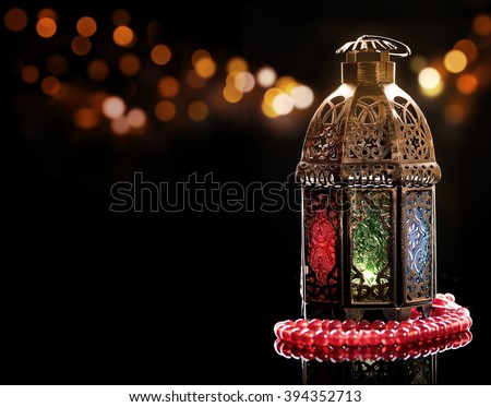 Vintage lantern with red rosary.\
Ramadan mood at night with light decoration in the background.