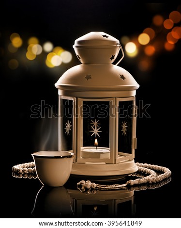 White lantern with Arabian coffee and rosary.\
Ramadan mood at night with light decoration in the background.
