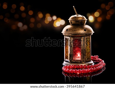 Vintage lantern with red rosary.\
Ramadan mood at night with light decoration in the background.