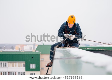 Industrial climber in uniform and helmet sitting on the roof preparing to the work in winter