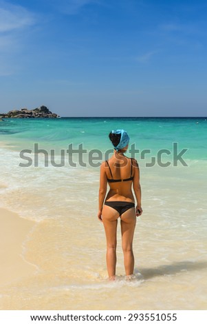 Young girl relaxes on the shore of the blue sea with white sand. Is back in a swimsuit.