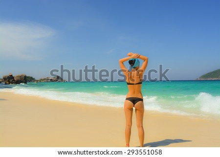 Young girl relaxes on the shore of the blue sea with white sand. Is back in a swimsuit.