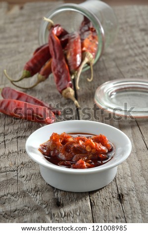 Red chili sambal sauce with dried red chilis in the background on rustic wood.