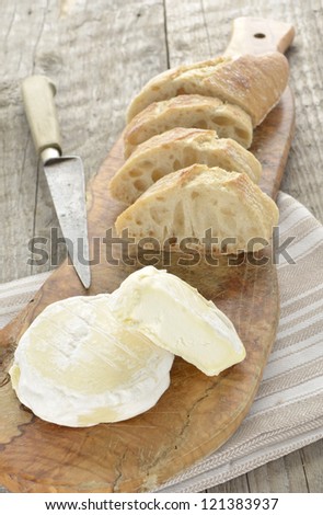 French St Marcellin soft cheese with baguette and old french knife on a rustic wooden board